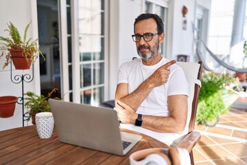 Middle age man using computer laptop at home pointing with hand finger to the side showing advertisement, serious and calm face