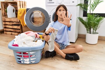 Poster - Young hispanic girl doing laundry holding socks doing stop gesture with hands palms, angry and frustration expression