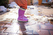 Child jumps on puddles in rubber boots at sunset lights in spring time