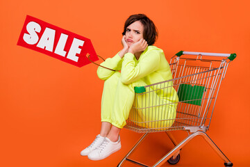 Sticker - Creative collage of unsatisfied girl sitting empty shelf supermarket shopping card isolated on orange color background