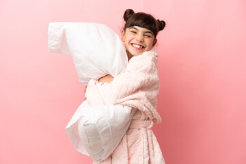 Wall Mural - Little caucasian girl isolated on pink background in pajamas and holding a pillow with happy expression