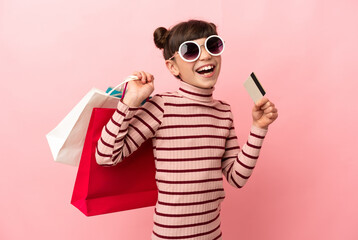 Wall Mural - Little caucasian girl isolated on pink background holding shopping bags and a credit card