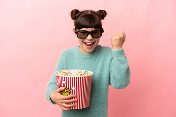 Wall Mural - Little caucasian girl isolated on pink background with 3d glasses and holding a big bucket of popcorns