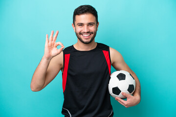 Wall Mural - Young football player Brazilian man isolated on blue background showing ok sign with fingers