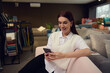 © Taras Grebinets - Interior designer- charming elegant brunette European woman in casual attire sitting on a stylish modern pink sofa and typing text on her mobile phone