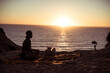 © Cavan Images - man sits alone on picnic rug with phone camera as sunsets over ocean