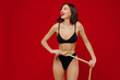 © ViDi Studio - Young slender thin slim fun woman 20s with perfect fit body wear black underwear hold measure tape on waist look overhead on workspace isolated on plain red background People female beauty concept.