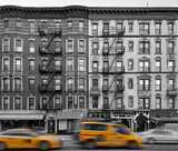 Fototapeta  - Yellow taxis driving past old apartment buildings in the East Village neighborhood of New York City in black and white