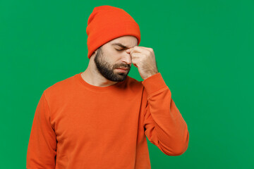 Wall Mural - Young sad puzzled minded pensive caucasian man 20s wear orange sweatshirt hat keep eyes closed rub put hand on nose think isolated on plain green background studio portrait. People lifestyle concept.