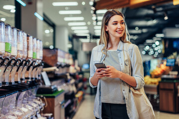 Wall Mural - Beautiful woman grocery shopping with cellphone