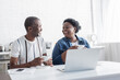 © LIGHTFIELD STUDIOS - retired african american husband and wife holding cups and looking at each other near laptop.