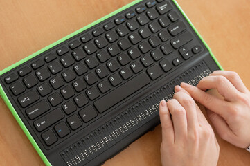 a blind woman uses a computer with a braille display and a computer keyboard. inclusive device.