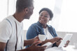 © LIGHTFIELD STUDIOS - smiling african american woman pointing at digital tablet and looking at senior husband with cup of coffee.