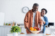 © LIGHTFIELD STUDIOS - senior african american man putting bowl with fruits on breakfast table near smiling wife.