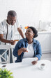 © LIGHTFIELD STUDIOS - senior african american man holding credit card while online shopping near happy wife pointing at digital tablet.