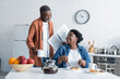 © LIGHTFIELD STUDIOS - cheerful and senior african american man holding cup and newspaper while looking at wife having breakfast.