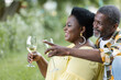 © LIGHTFIELD STUDIOS - romantic senior african american man pointing away near happy wife with glass of wine.