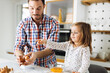 © Goran - Cute girl and her father making cookies while baking in the kitchen