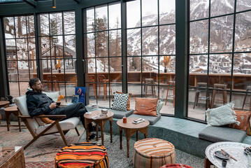 Wall Mural - Contemplating man having coffee while looking at mountains from window in resort