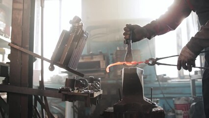 Wall Mural - Man blacksmith takes a piece of metal out of a furnace - puts it on the form on anvil and starts hitting the detail with a hammer