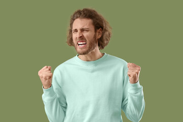 Wall Mural - Angry young man in sweatshirt on green background