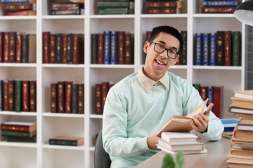 Wall Mural - Male Asian student reading book at table in library