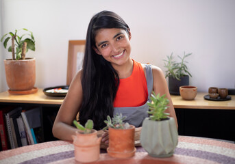 young mexican woman smiling with plants and pots at home and gardening outfit