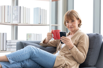 Wall Mural - senior woman using smartphone and holding a cup of coffee