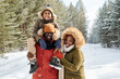 © pressmaster - Cheerful family of three in warm winterwear spending day in winter forest or park among firtrees and pines covered with snow