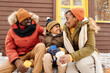 © pressmaster - Cute happy boy in winterwear sitting between his parents on porch of their family country house, having hot tea and chatting