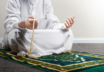 Poster - Muslim man praying with prayer beads on his hands while sitting on the prayer rug