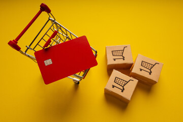 Shopping cart, delivery boxes and red credit card on yellow background