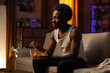 A muscular handsome man is spending an evening alone on the couch in the living room, a boy with afro is holding a bowl of chips in his hands, eating a snack, next to him a box of pizza