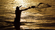 A fisherman throwing his net in shallow sea at dawn