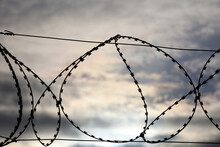 Barbed Wire On Background Of Dramatic Sky With Clouds. Concept Of Boundary, Prison, War Or Immigration