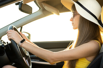 Wall Mural - Young woman driver in summer yellow dress and straw hat driving a car.