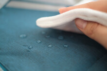 Hand Wipes Drops Of Water From A Cloth. Water Drops On Waterproof Textile Material. Short Depth Of Field. Waterproof Fabric On Sofa.