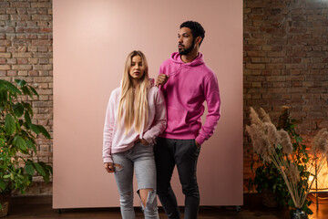 Wall Mural - Fashion studio portrait of a happy young couple in hoodie posing over pink background.