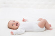 © inarik - Happy Smiling Baby lying on back in White Bed. Active Playful Baby Boy in White Cotton Bodysuit. Laughing Infant Child in babies Onesies looking at Camera. Three month Small Kid at Home