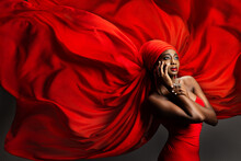 African Black Woman In Red Silk Headscarf. Fashion Dark Skinned Model Portrait In Turban With Golden Jewelry In Hijab Flying Chiffon Fabric Over Gray Background. Stylish Arab Beauty Women Headwear