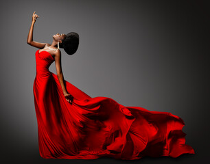Wall Mural - Fashion African Woman in Silk Dress dancing. Dark Skinned Model with Black Afro Hair in Long Evening Red Gown with Tail Fabric flying over Gray Background. Women Luxury Clothing Side View