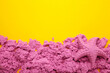 Pink kinetic sand for children, development and play at home with multi-colored sandbox molds on yellow background.