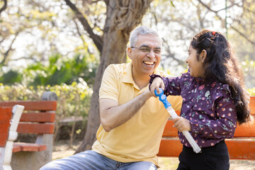 Wall Mural - Senior man with granddaughter having fun blowing bubbles at park