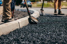 Road Workers With Shovels In Their Hands Throw Forked Asphalt On A New Road. Road Service Repairs The Highway