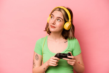 Young caucasian woman playing with a video game controller isolated on pink background dreaming of achieving goals and purposes