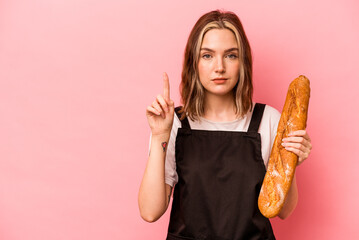 Young baker caucasian woman isolated on pink backgroundshowing number one with finger.