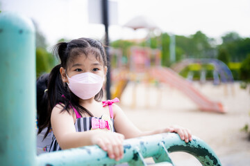 Portrait cute kid girl playing exercise equipment at playground. Child 5 years old wearing 4D face mask at outdoors. In summer or spring time. Protection toxic dust PM2.5 and spread coronavirus.