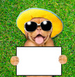 Happy mastiff puppy wearing sunglasses and summer hat lying on its back on summer green grass and holds empty board. Top down view. Empty space for text