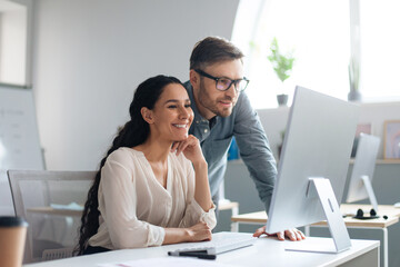 Smiling male and female employees discussing business project, using computer at company office, copy space