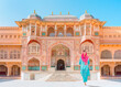 An Indian woman dressed in traditional costume walks between columns - Columned hall of Amber fort - Jaipur, Rajasthan, India